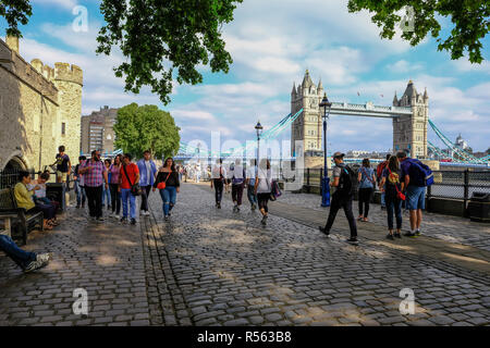 Tower, London, Großbritannien - 8. Juni 2018: Cobbed Steine und Menschen neben dem Tower von London mit Tower Bridge im Hintergrund bummeln. An einem sonnigen genommen
