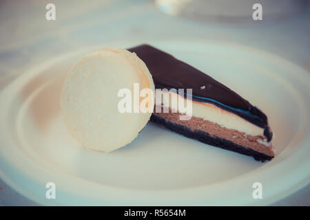 Stück Schokolade - Vanille Mousse Cake mit Glsaz von Schokolade und weisse Makronen auf einem weißen Teller. Stockfoto