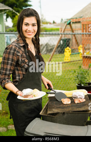Hübsche Frau lächelnd Grillrost Steaks grillen Garten essen Stockfoto