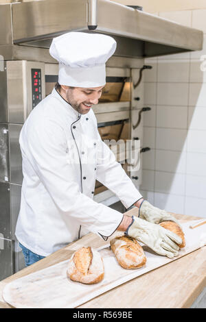 Lächelnd Bäcker in der Nähe von mit frisch gebackenem Brot auf Holz- zähler Backofen Stockfoto