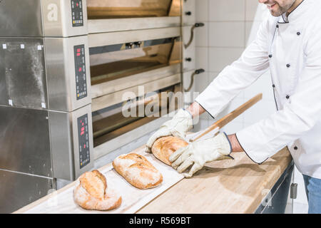 Bäcker in der Nähe von Ofen mit heißem gebackene Brot auf Holz- Zähler Stockfoto