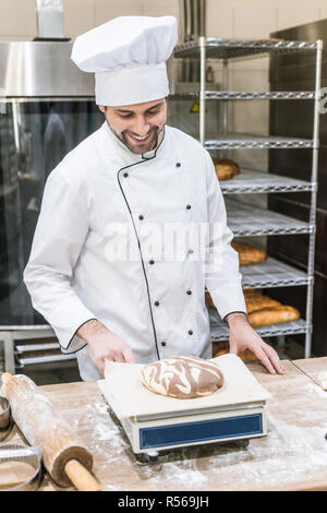 Lächelnd baker Wiegen rohen Teig auf Küchenwaagen Stockfoto