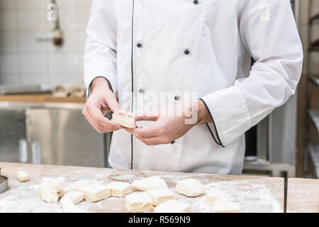 7/8-Ansicht von Baker in Uniform Köche kochen Teig auf hölzernen Tisch Stockfoto