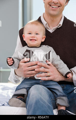 Baby Junge saß auf seiner Väter Knie Stockfoto