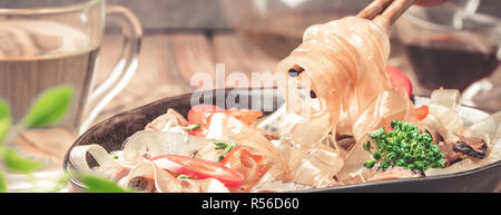 Hand mit Stäbchen nehmen Sie heißen asiatischen würzigen Gericht Dicke schneiden Glasnudeln Bohnen süß saurer Soße Fleisch Gemüse Paprika Brokkoli in Schüssel Lauch auf Küche Stockfoto
