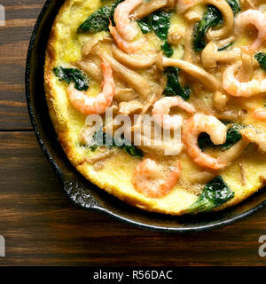 Nahaufnahme von Omelette (Pilze und Spinat frittata mit Shrimps) in der Pfanne auf Holz- Hintergrund. Ansicht von oben, flach Stockfoto