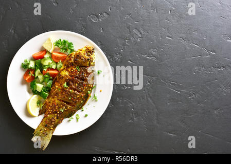 Gebackener Fisch mit gesunden Salat von frischem Gemüse auf die Platte über der schwarzen Stein Hintergrund mit Kopie Raum. Top Aussicht, flach Stockfoto