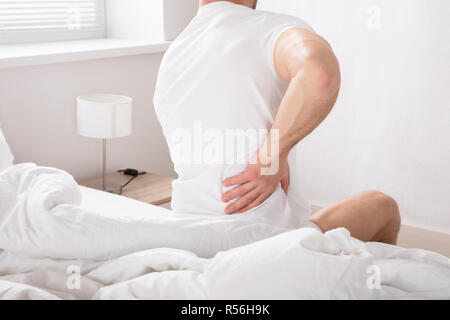 Mann sitzt auf dem Bett, Rückenschmerzen Stockfoto