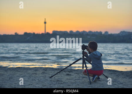 Kreative Kind, junge Fotografen (ein kleiner Junge) mit einer Kamera Landschaft Bilder bei Sonnenuntergang Stockfoto