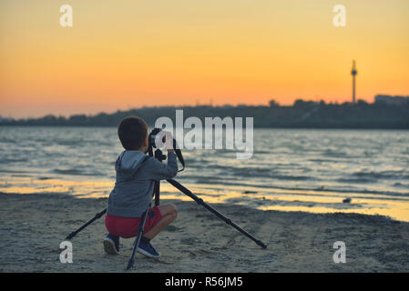 Kreative Kind, junge Fotografen (ein kleiner Junge) mit einer Kamera Landschaft Bilder bei Sonnenuntergang Stockfoto