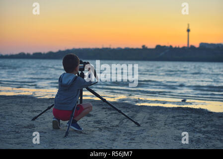 Kreative Kind, junge Fotografen (ein kleiner Junge) mit einer Kamera Landschaft Bilder bei Sonnenuntergang Stockfoto