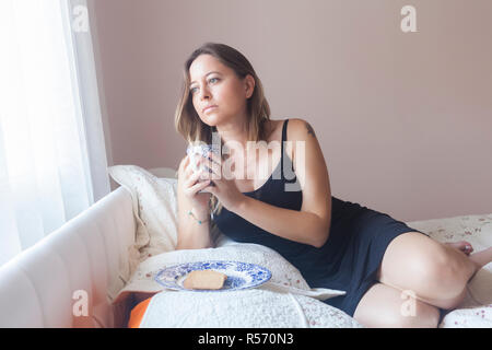 Entspannt liegende Frau auf ihrem Bett Blick durch Fenster holding Coffee Mug Stockfoto