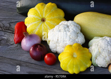 Still-Leben von Gemüse der Saison auf einem rustikalen Holztisch. Grüne Zucchini, gelben Kürbis, Tomaten, Blumenkohl, Paprika und Zwiebeln. Stockfoto