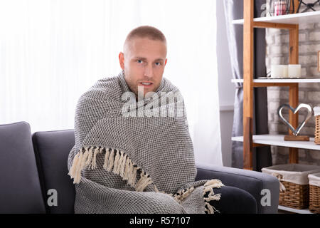 Kranke junge Frau mit Decke auf dem Sofa sitzen Stockfoto