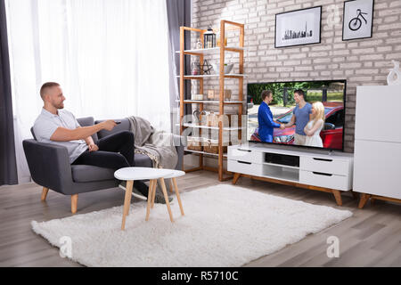 Mann sitzt auf einem Sofa Fernsehen zu Hause beobachten Stockfoto