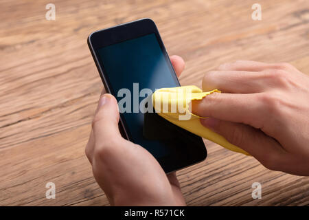 Mann Reinigung Mobiltelefon mit gelben Tuch über Holz- Schreibtisch Stockfoto