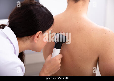 Ärztin Untersuchung pigmentierter Haut des Menschen zurück Mit Dermatoskop Stockfoto