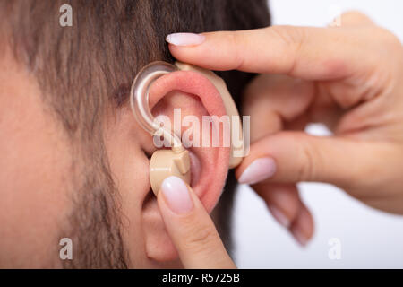 In der Nähe von einem Arzt Hand einfügen Hörgerät im Ohr des Männlichen Patienten Stockfoto