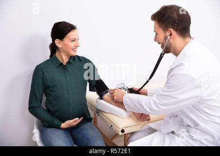 Junge männliche Arzt Kontrolle Blutdruck von Lächelnd weibliche Patienten in der Klinik Stockfoto