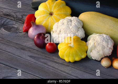 Still-Leben von Gemüse der Saison auf einem rustikalen Holztisch. Grüne Zucchini, gelben Kürbis, Tomaten, Blumenkohl, Paprika und Zwiebeln. Stockfoto