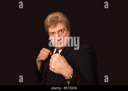 Studio shot der verärgerten älterer Geschäftsmann mit Faust heben gegen den dunklen Hintergrund Stockfoto