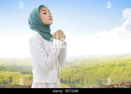 Hübsche asiatische Muslimin hijab tragen heben die Hand und Beten Stockfoto