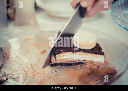 Weibliche hand mit einem Messer schneiden Schokolade - Vanille Mousse Cake mit Glsaz von Schokolade und weisse Makronen. Stockfoto