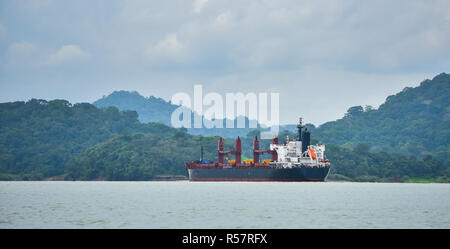 Ein großes Frachtschiff macht seinen Weg durch den Panamakanal Wasserstraßen, auf jeder Seite zwischen den Schleusen mit grünen Regenwald Dschungel flankiert wird. Stockfoto