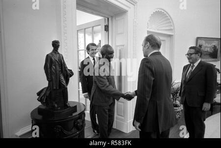 4/19/1975 - Foto von Präsident Gerald R. Ford, Außenminister Henry Kissinger, und Chef des Protokolls Henry Catto Begrüßung Präsident Kenneth Kaunda von Sambia im Oval Office Stockfoto