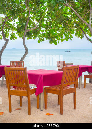 Holz- Tisch mit roten Tischdecke auf den Sandstrand mit dem Long-tail-Boot und Marine vertikalen Stil. Stockfoto