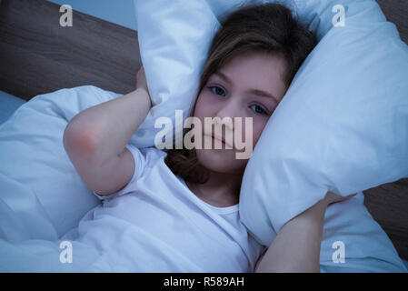 Mädchen, die ihre Ohren mit Kissen beim Schlafen Stockfoto