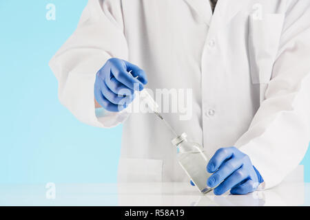 Die Hand in einer blauen Handschuh Holding Spritze auf blau Stockfoto