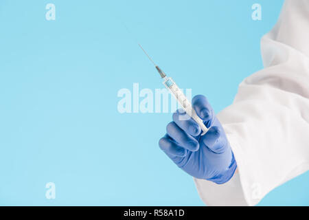 Die Hand in einer blauen Handschuh Holding Spritze auf blau Stockfoto