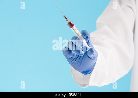 Die Hand in einer blauen Handschuh Holding Spritze auf blau Stockfoto