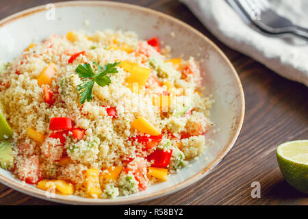 Couscous Salat mit frischen Rote und gelbe Paprika, Avocado, Tomaten und Kalk. Das Konzept der vegetarische und gesunde Ernährung. Stockfoto