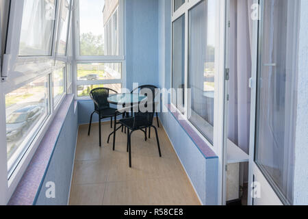 Ein Tisch und drei Stühle auf dem Balkon in der Wohnung eines mehrstöckigen Mehrfamilienhauses Stockfoto