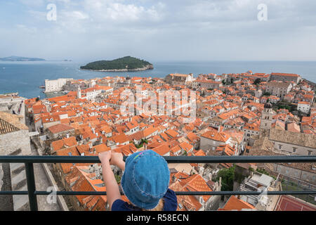 Kleines Mädchen wearnig blauen Hut auf der alten Stadtmauer in Dubrovnik mit Blick auf die historische Stadt unten, Kroatien Stockfoto