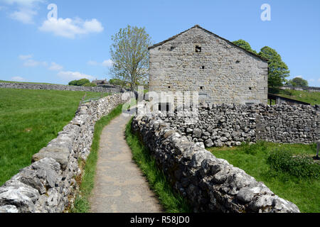 Ein kies Fußweg zwischen Trockenmauern und neben einem Häuschen entlang der Dales Weg Wanderweg, in Yorkshire, England, Vereinigtes Königreich. Stockfoto