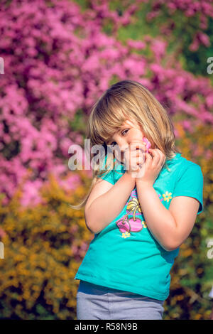 Little Girl posiert vor bunten rosa und gelb blühende Blumen im Frühling Stockfoto