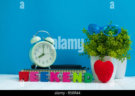 Wochenende Buchstaben text und Notebook Papier, Wecker und wenig Deko Baum in weiße Vase auf hölzernen Hintergrund, hallo Wochenende Urlaub Konzept ide Stockfoto