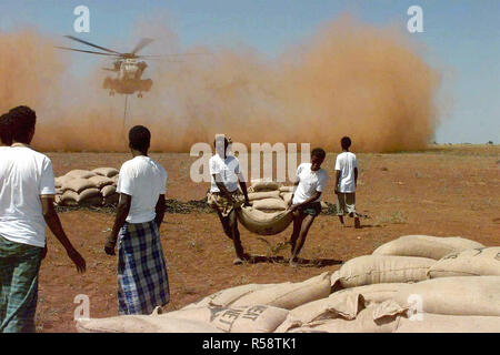 1993 - Im Vordergrund somalische Männer große Taschen von Weizen und legen Sie sie in den ordentlichen Stacks. Im Hintergrund ein US Marine CH-53 Sea Stallion Hubschrauber steht vor der Kamera und schwebt über fünfzig Meter über dem Boden. Eine große Wolke der roten Staub wird durch den Hubschrauber Rotor waschen getreten. Die "Roten Löwen" der Marine schwere Hubschrauber Geschwader 363 in Tustin, Kalifornien fliegen die Hubschrauber. Diese Mission ist in der direkten Unterstützung der Operation Restore Hope. Stockfoto