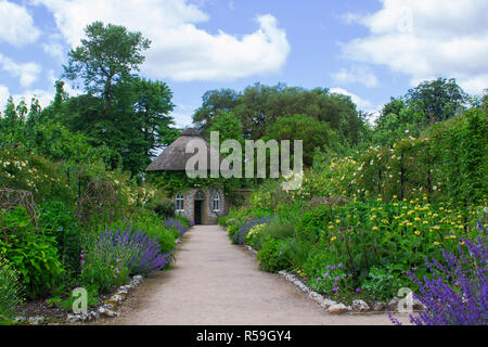 Das 19. Jahrhundert strohgedeckten runden Haus, umgeben von schönen Blumenbeeten und Schotterwege, das in der ummauerten Garten in West Dean Gärten in West Sussex Stockfoto