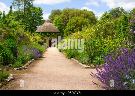 Das 19. Jahrhundert strohgedeckten runden Haus, umgeben von schönen Blumenbeeten und Schotterwege, das in der ummauerten Garten in West Dean Gärten in West Sussex Stockfoto