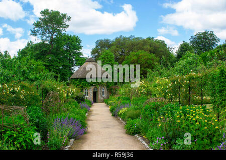 Das 19. Jahrhundert strohgedeckten runden Haus, umgeben von schönen Blumenbeeten und Schotterwege, das in der ummauerten Garten in West Dean Gärten in West Sussex Stockfoto