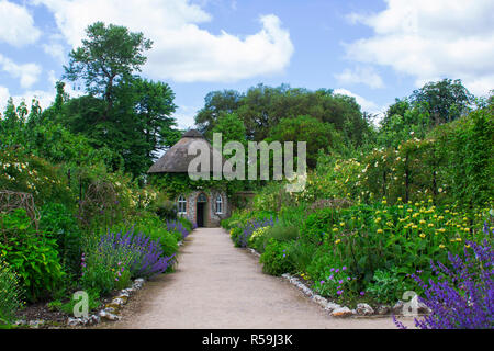 Das 19. Jahrhundert strohgedeckten runden Haus, umgeben von schönen Blumenbeeten und Schotterwege, das in der ummauerten Garten in West Dean Gärten in West Sussex Stockfoto