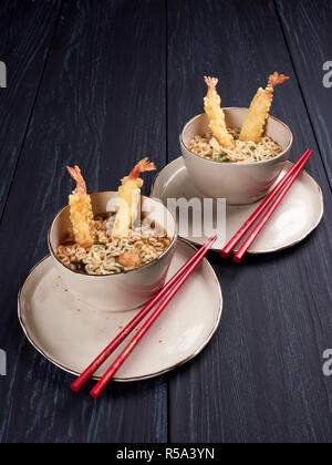 Zwei Schalen mit Tempura udong Nudeln mit Garnelen temputa, in beige Schüsseln mit roten Stäbchen, auf dunkelblauem Hintergrund Stockfoto