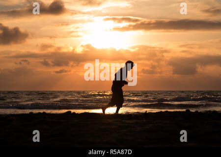 Mann läuft und denkt bei Sonnenuntergang am Strand Stockfoto