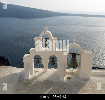 Ein Blick von der Stadt Oia über die vulkanische Caldera in Santorin, Griechenland. Ein Glockenturm der ägäischen Architektur im Zentrum. Stockfoto