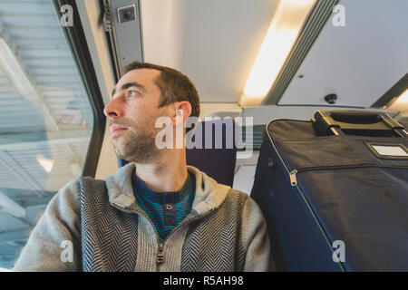 Junger Mann auf Reisen im zug und schaut aus dem Fenster Stockfoto