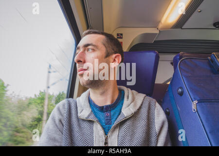 Junger Mann auf Reisen im zug und schaut aus dem Fenster Stockfoto